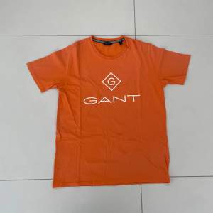 Säljer en snygg orange t-shirt från GANT i bomull. Den har en klassisk passform med korta ärmar och en rund halsringning. Perfekt för sommardagar eller avslappnade tillfällen. GANT-loggan är tryckt i vitt på framsidan. Skicka ett meddelande vid intresse! 🧡