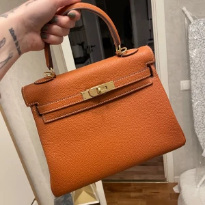 H Kelly Väska - Använd en gång, i en orange fin färg med gulddetaljer. Kommer med axelrem och dustbag. Nypris 2000 kronor! 🙂