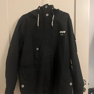 Svart vinterjacka från Dope - Säljer en svart jacka från Dope i storlek L. Den är vattentät och andas bra med 15 000 mm och 15 000 g/m2/24h. Jackan har dragkedja och huva, perfekt för höst och vinter. Tillverkad med 60% växtbaserade fibrer och är fluorkarbonfri. Tvättad innan den skickas