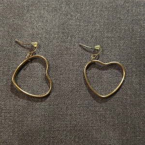 Guldiga hjärtformade örhängen - Säljer ett par superfina guldiga örhängen i form av hjärtan. Perfekta för att ge en romantisk touch till din outfit. De är lätta och bekväma att bära hela dagen. Passar både till vardags och fest! 💖