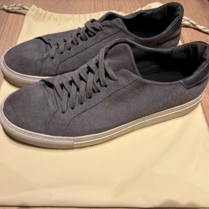  Axel Arigato skor - Säljer ett par stilrena grå sneakers från Axel Arigato i mocka. Perfekta för både vardag och festliga tillfällen. Skorna är i bra skick och kommer med originalpåse.