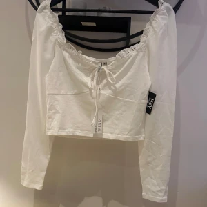 Vit topp - Säljer denna fina vita topp från Nelly, aldrig använd, prislappen är kvar, storlek M.