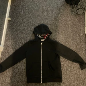 Burberry zip hoodie - En svart burberry zip hoodie med ett svart och rutigt tema, koftan är stilren och passar alla stiler. Pris kan diskuteras. Storlek S men passar även M