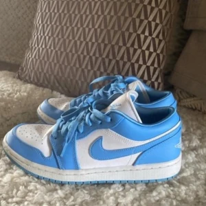 Nike Air Jordans i blått och vitt - Snygga Nike Air Jordans i en fräsch blå och vit färgkombination. Skorna har klassisk snörning och den ikoniska Air Jordan-loggan på hälen. Perfekta för dig som vill ha en stilren och sportig look.