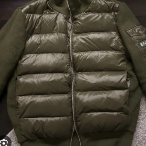 Olivgrön pufferjacka från Bvaldi - Snygg olivgrön pufferjacka från Bvaldi med dragkedja och quiltad design. Jackan har långa ärmar och en cool patch på ärmen. Perfekt för kyligare dagar. Andvänd fåtalgånger då den inte passa mig. Kan gå ner i pris vid snabb affär.