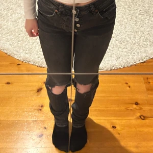 Svarta jeans med slitningar - Snygga svarta jeans med slitningar på knäna och knappar framtill. De är högmidjade och har en tight passform som framhäver figuren. Perfekta för en trendig look. Jag är ca 160 cm