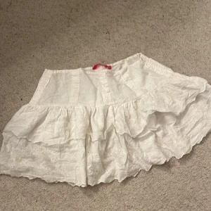 Vit kjol med volang från Unisa - Charmig vit kjol från Unisa med volangdetaljer. Kjolen har en elastisk midja och är perfekt för en somrig look. Den är tillverkad i ett lätt och luftigt material som ger en skön känsla.