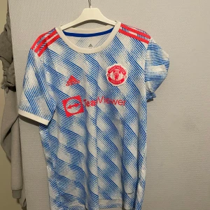 Manchester United fotbollströja -  Manchester United fotbollströja  i vitt och blått med röda detaljer.  Size M. Passar perfekt för sommarn, sporta eller som en vanlig tröja. Den är aldrig använd. Köpt i slutet av sommaren. Nypris 999 från Adidas