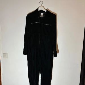 Svart jumpsuit från H&M Studio - Snygg svart jumpsuit från H&M Studio med dragkedjor på bröstfickorna och en klassisk krage. Perfekt för en stilren look.🥰🥰🥰