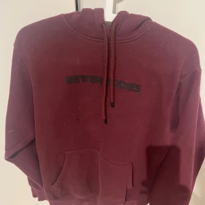 Vinröd hoodie från Better Bodies - Säljer en vinröd hoodie från Better Bodies med svart text på bröstet. Den har en justerbar dragsko i huvan och en praktisk magficka. Perfekt för en avslappnad stil.