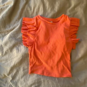 Korall färgad topp från zara - Säljer en snygg orange ribbad topp med volangdetaljer på ärmarna. Perfekt för att liva upp garderoben med lite färg. Toppen har en tight passform och är tillverkad i ett mjukt material. Storlek s