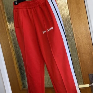 Röda träningsbyxor från Palm Angels - Snygga röda träningsbyxor från Palm Angels som jag ej använder då de inte är riktigt min stil, pris kan diskuteras. Kan även sälja ihop med andra byxor från samma märke. 