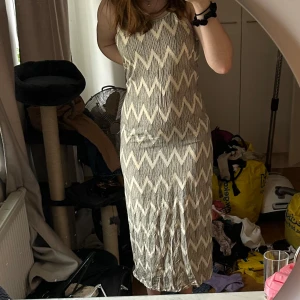Mönstrad långklänning med slits - Säljer en snygg långklänning med ett coolt sicksackmönster i beige och svart. Klänningen är ärmlös och har en slits på båda sidorna som ger en extra touch. Perfekt för en avslappnad stil. Säljer då jag inte gillar längden och den inte kommit till användning. Vet inte storlek eller varumärke då det inte finns någon lapp men gissar att den är i strl S.