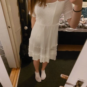 Vit klänning - Söt vit klänning med spetsdetaljer och korta ärmar. Klänningen har en luftig passform och volanger på kjolen. Perfekt för student eller skolavslutning. St 152 med sitter som xxs. Använd fåtal gånger