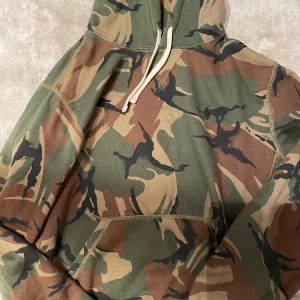 Camouflage hoodie från Polo Ralph Lauren - Säljer en cool camouflage hoodie från Polo Ralph Lauren. Den har en klassisk design med huva och dragsko, perfekt för en avslappnad stil. Hoodien är i gröna och bruna toner med ett mönster som ger en tuff look. Perfekt för höst och vinter! KOM MED BUD