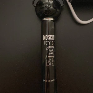 Moschino Toy Boy Eau de Parfum - Säljer en Moschino Toy Boy Eau de Parfum i en stilren svart flaska med en nallebjörnsdesign. Flaskan rymmer 10 ml och har en unik och lekfull design som sticker ut. Perfekt för den som gillar att ha en doft med karaktär och stil. Pris kan diskuteras 
