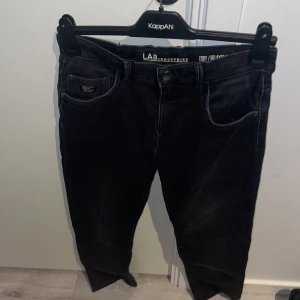 Svarta jeans från LAB Industries - Snygga svarta jeans från LAB Industries med klassisk femficksdesign. De har en knapp och dragkedja framtill samt bälteshällor. Perfekta för en stilren look. Storlek 158 passar 164