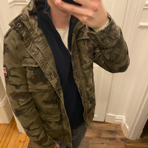 Fodrad Field jacka - Säljer en fodrad Field jacka i camo från Superdry. Jackan har en militärinspirerad look med flera fickor. Den är fodrad med mjuk teddy för extra värme. Perfekt för höst och vår! Han på bilden är ca 182, tveka inte att kontakta vid eventuella frågor 😀
