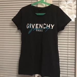 Svart Givenchy t-shirt  - Snygg svart Givenchy t-shirt med vit och blå text på bröstet.  T-shirten har korta ärmar och en rund halsringning. 