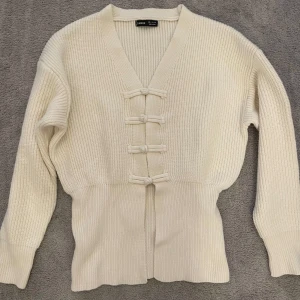 Vit ribbad kofta  - Säljer en stilren vit ribbad kofta med knytning framtill. Koftan har en v-ringad design och långa ärmar. Aldrig använd