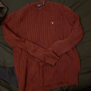 Rostfärgad stickad tröja från Gant - Säljer en snygg rostfärgad stickad tröja från Gant. Tröjan har ett diskret kabelstickat mönster och Gant-loggan broderad på bröstet. Perfekt för kyligare dagar med sin långa ärmar och ribbade kanter.