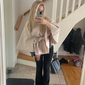 Beige kappa med knytband - Snygg beige kappa med knytband i midjan och en knappdetalj vid halsen. Den har vida ärmar och passar perfekt för höst och vår. Kappan är från missäy💕använd få gånger! så väldigt fint skick
