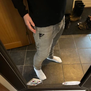 Grå Replay Anbass jeans - Snygga grå jeans från Replay, modell Anbass. De har en modern slim passform och är tillverkade i ett bekvämt material. Perfekta för en stilren look med klassiska detaljer som dragkedja och knappar.