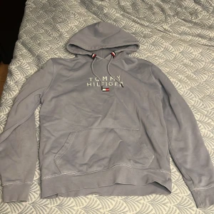 Ljus blå hoodie från Tommy Hilfiger - Säljer en stilren ljus blå hoodie från Tommy Hilfiger i ekologisk bomull. Den har en klassisk design med logotypen broderad på bröstet och justerbar huva med snören i rött, vitt och blått. Perfekt för en avslappnad look. Storlek L men passar även M