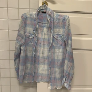 Rutig skjorta från Cappuccini - Säljer en stilren tunn rutig skjorta från Cappuccini i ljusblått, vitt och rosa. Skjortan har långa ärmar och två bröstfickor med knappar. Perfekt för sommaren eller stranden☀️