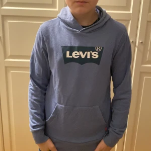 Blå hoodie från Levi's - Säljer en snygg blå hoodie från Levi's med deras ikoniska logga på bröstet. Tröjan har en klassisk passform med långa ärmar och en praktisk ficka framtill. Perfekt för en avslappnad stil.