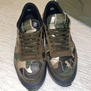 Valentino Garavani sneakers - Valentino Garavani sneakers med camouflagemönster i gröna och beige toner. Skorna kommer med snören och har röda detaljer på hälen. Storlek 42/43. I använt skick men fungerar precis lika bra som nya. Skriv om du har frågor eller funderingar! 