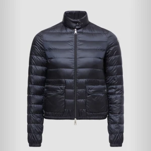 Svart dunjacka från Moncler - Säljer en stilren svart dunjacka från Moncler. Jackan har en hög krage och dragkedja framtill. Den är quiltad med två framfickor och Moncler-loggan på ärmen.storlek 2