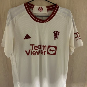 Manchester United tredjetröja  - Säljer Uniteds tredje tröja  i storlek M. Tröjan har korta ärmar och är i mycket bra skick. Den har röda detaljer och tryck med 'Team Viewer' på framsidan och 'Garnacho 17' på baksidan. Perfekt för fotbollsfans!