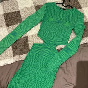 Grön midi klänning, S - Grön klänning med långa ärmar och utsnitt på sidorna. Klänningen är figursydd och har en mjuk, stickad struktur.