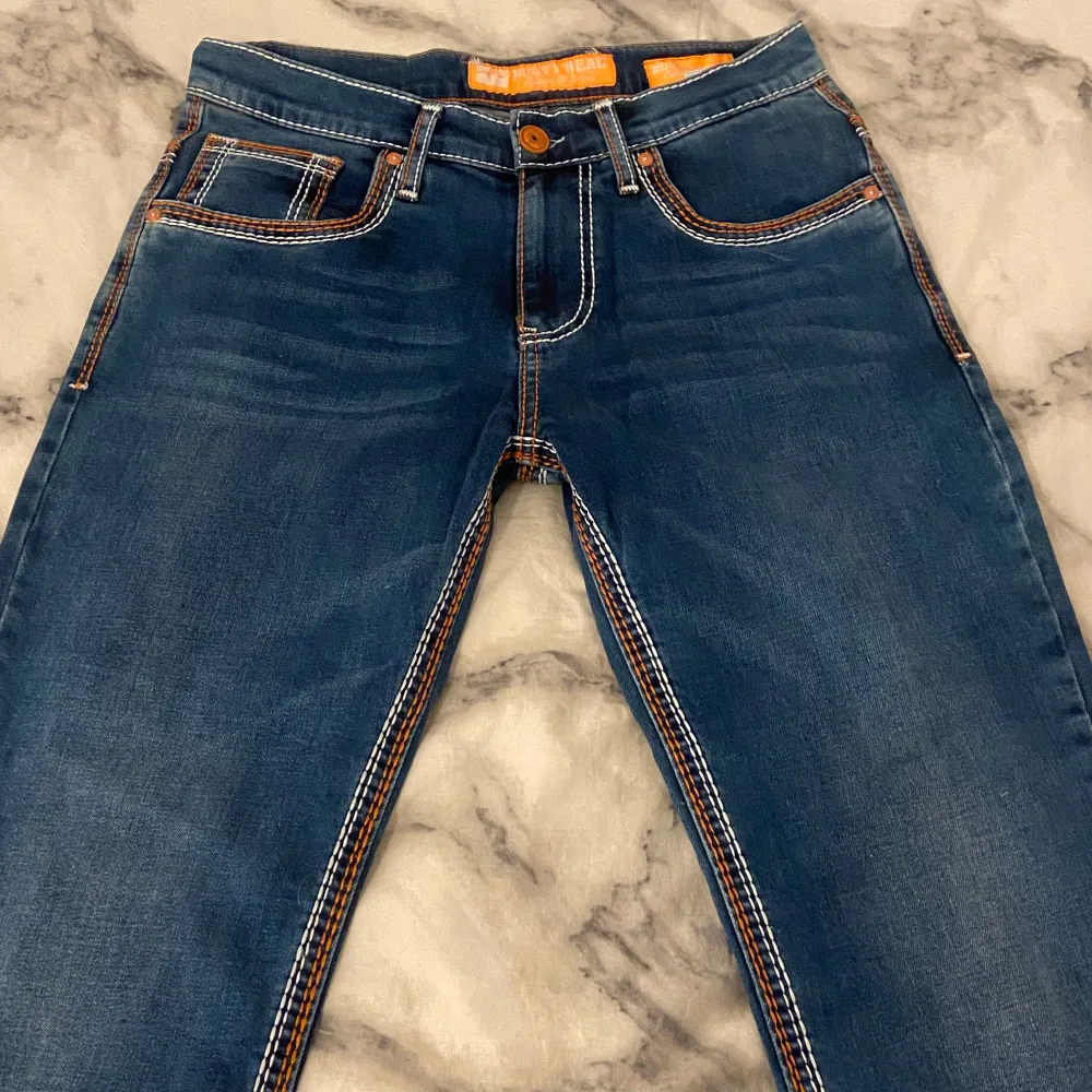 Säljer ett par snygga straightleg jeans från Rusty Neal. De har en cool kontrastsöm i orange och vit som verkligen poppar. Klassisk femficksdesign med en knapp och dragkedja fram. Perfekta för vardagsbruk eller en avslappnad utekväll. Passar bra till både sneakers och boots! 🧡 DM vid frågor osv!. Jeans & Byxor.