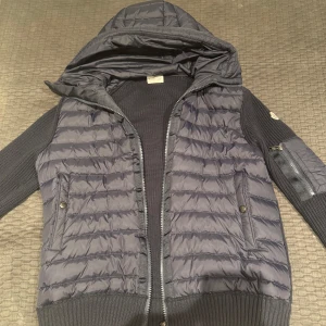 Svart cardigan jacka från Moncler - Säljer en snygg svart cardigan  jacka från Moncler. Den har en huva och dragkedja framtill. Ärmarna är ribbade och det finns en praktisk ficka med dragkedja på ena ärmen. Perfekt för höst och vår!. Pris går att diskutera. Storlek L men funkar för personer me M också 