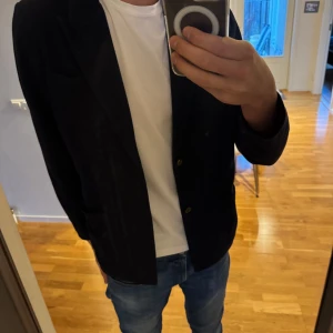 Mörkblå blazer/kofta från John Henric - Säljer en stilren mörkblå blazer/kofta från John Henric i storlek M. Perfekt för både fest och vardag. Kavajen har två knappar och en klassisk passform. Materialet känns bekvämt och ger en elegant look. Passar bra till jeans eller kostymbyxor.