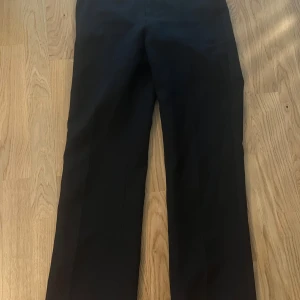 Svarta kostymbyxor från Nelly - Säljer ett par stilrena svarta byxor från Nelly i storlek 32. De har en klassisk design med en rak passform som passar perfekt för både vardag och fest. Byxorna är i mycket bra skick och kan enkelt matchas med olika toppar för en snygg look.