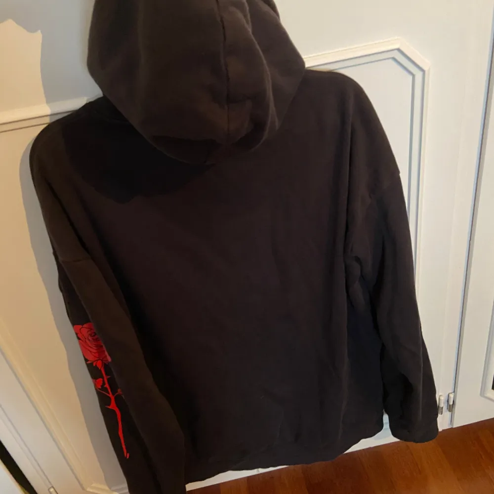 En svart hoodie med texten ”HRTBRKR” på och röda rosor vid ärmen. Använd ett par gånger men inga tecken på skador eller slitage.. Hoodies.