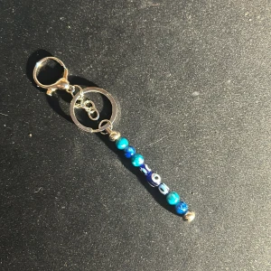 Nyckelring med blå pärlor - Snygg nyckelring med en rad av blå pärlor i olika nyanser och mönster. Den har en silverfärgad ring och karbinhake för enkel fastsättning. Perfekt accessoar för att ge dina nycklar lite extra stil!