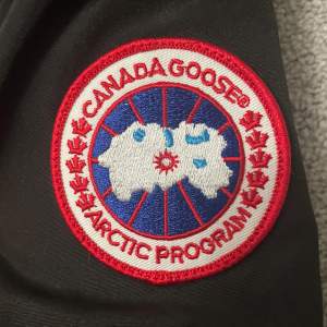 Säljer en svart Canada Goose dunjacka i mycket bra skick. Jackan har en avtagbar päls på huvan och är perfekt för kalla vinterdagar. Den är långärmad med dragkedja och knappar framtill. Supervarm och stilren! Helt ny 