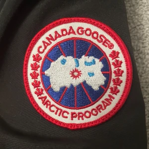  Canada Goose jacka  - Säljer en svart Canada Goose dunjacka i mycket bra skick. Jackan har en avtagbar päls på huvan och är perfekt för kalla vinterdagar. Den är långärmad med dragkedja och knappar framtill. Supervarm och stilren! Helt ny 