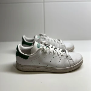 Adidas Stan Smith sneakers - Säljer ett par klassiska Adidas Stan Smith sneakers i vitt med gröna detaljer. Skorna är i använd men bra skick. Perfekta för en avslappnad stil och passar till det mesta. Storlek 40 och 2/3 