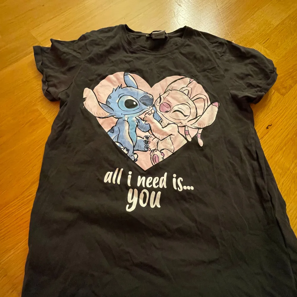 Säljer en svart t-shirt från Disney med ett gulligt tryck av två karaktärer i ett hjärta och texten 'all I need is... you'. Perfekt för vardagsbruk eller som en söt present. T-shirten är i bra skick och gjord av mjukt material.. T-shirts.