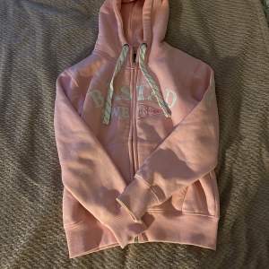 Säljer en superfin rosa hoodie från Nautiska Magasinet. Den har en dragkedja framtill och en mysig huva med snören. Texten 'Båstad Sweden' är tryckt på framsidan. Använd ett fåtal gånger, så den är i mycket bra skick. 💖