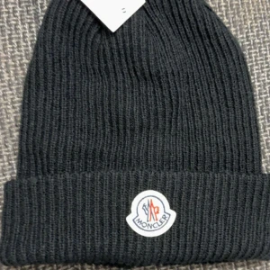 Svart stickad mössa från Moncler - Snygg och stilren svart stickad mössa från Moncler. Perfekt för kalla dagar med sitt ribbade material och klassiska design. Den har en uppvikt kant och Monclers logga framtill. Passar både till vardags och mer uppklädda tillfällen.