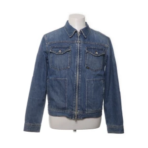 Blå jeansjacka med dragkedja - Säljer en klassisk blå jeansjacka i nytt skick. Den har en dragkedja framtill och två bröstfickor med knappar. Jackan är en kort modell och därför passar snyggt till byxor med hög midja. Inga täcken på användning eller dylikt.