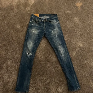 Blå jeans från DONDUP - Säljer ett par snygga blå jeans från George i bra skick. De har en cool slitningseffekt och är perfekta för en avslappnad stil. Jeansen har en klassisk femficksdesign och en bekväm passform. Perfekta för både vardag och fest!