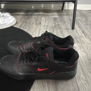 Svarta Nike sneakers med röda detaljer - Säljer ett par svarta Nike sneakers i mycket bra skick. De har snygga röda detaljer och klassisk snörning. Perfekta för både vardag och träning. Skorna är bekväma och stilrena, vilket gör dem till ett måste i garderoben.