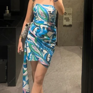 Färgglad axelbandslös klänning - Säljer en superfin axelbandslös klänning med ett färgglatt mönster i blått, grönt och rosa. Klänningen har en omlott-design och en liten slits på sidan, perfekt för sommarens fester. Den är i bra skick och passar perfekt för en kväll ute eller en sommarfest. 🌸